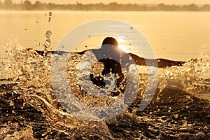 Strong man in silhouette swimming at lake in butterfly style