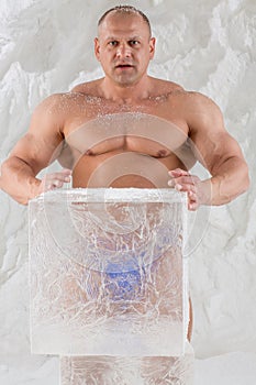 A strong man with snow on body in studio with ice