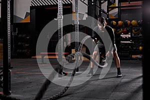 Strong man in sportive shorts doing battle ropes exercise at crossfit gym