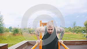 A strong man with tattoos pulling up on parallel bars on a sports ground