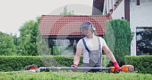 Strong man in uniform using electric hedge trimmer for shaping shrubs.