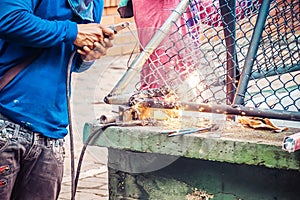 A strong man is a welder in a blue T-shirt,and welders leathers, a metal product is welded with a welding machine in the outdoor