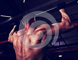 Strong masculine man athlete doing pull ups o dark fitness club background. Closeup