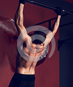 Strong masculine man athlete doing pull ups o dark fitness club background. Closeup portrait