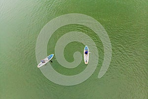 Strong men floating on a SUP boards in a beautiful bay on a sunny day. Aerial view of the men crosses the bay using the