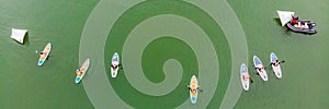 Strong men floating on a SUP boards in a beautiful bay on a sunny day. Aerial view of the men crosses the bay using the