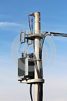 Strong metal electric power transformer with grey utility box mounted on high concrete utility pole and connected with electrical