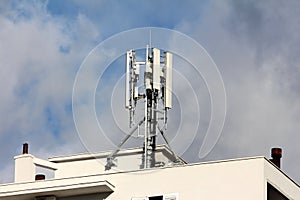 Strong metal pole with multiple cell phone antenna transmitters mounted on top of white business building next to rusted chimneys