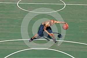 Strong muscular african-american male basketball player training at street public stadium, sport court or palyground