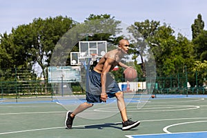 Strong muscular african-american male basketball player training at street public stadium, sport court or palyground