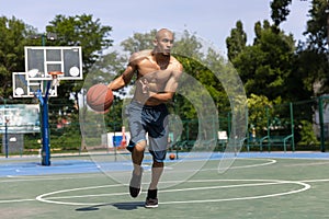 Strong muscular african-american male basketball player training at street public stadium, sport court or palyground