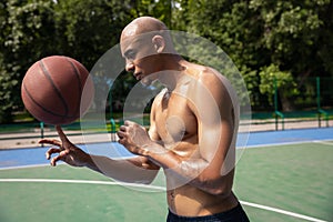 Strong muscular african-american male basketball player training at street public stadium, sport court or palyground