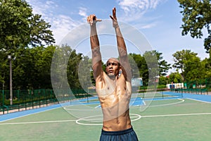 Strong muscular african-american male basketball player training at street public stadium, sport court or palyground