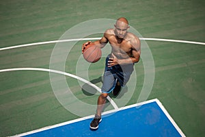 Strong muscular african-american male basketball player training at street public stadium, sport court or palyground