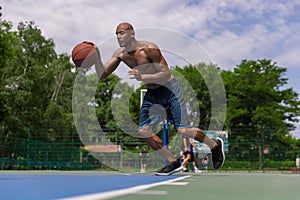 Strong muscular african-american male basketball player training at street public stadium, sport court or palyground