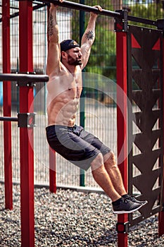 Strong Muscular bearded man doing abdominal exercise on horizontal bar in summer park. fitness, sport, exercising