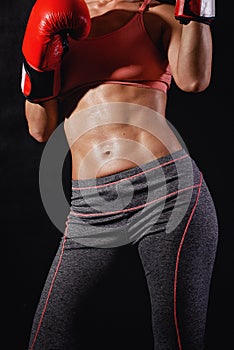 Strong muscular female body with six pack and with boxing gloves on a black background