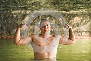 Strong muscular man bathe swim in outdoor cave, dirty hot springs. Thermal water bath pool. Healthy natural clay. Yellow