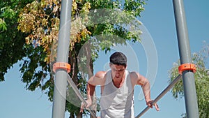 A strong muscular man does a push-up exercise on the push ups bars. Handsome guy workout on the sports ground in the city park