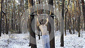 Strong and muscular man doing exercises on horizontal bar at winter forest. Young sportsman muscling up at beautiful