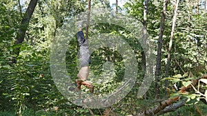 Strong muscular man doing a handstand in a forest. Muscular male fitness guy doing stunts on log at the wood. Athlete