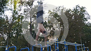 Strong muscular man doing a handstand in a park. Fit muscular male fitness guy doing stunts on horizontal bars outdoor