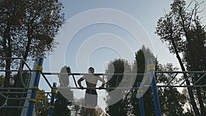 Strong muscular man doing muscle ups in a park. Young athlete doing chin-ups on horizontal bars outdoor. Fitness