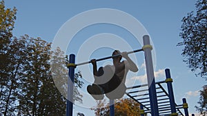 Strong muscular man doing pull ups in a park. Young athlete doing chin-ups and performs exercises on horizontal bars