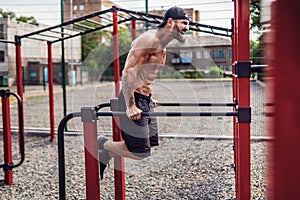 Strong muscular man doing push-ups on uneven bars in outdoor street gym
