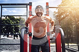 Strong muscular man doing push-ups on uneven bars in outdoor street gym