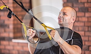 Strong muscular man exercising with trx facilities in gym or workout center