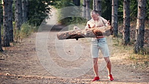 Strong muscular man lifting a log on a forest road