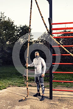 Strong muscular man wearing a workout breathing mask getting ready to climb a rope outdoors