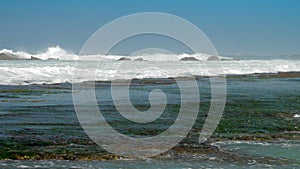 Strong ocean waves crash into brown rocks with white foam