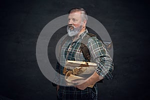 Strong old man with bag and stack of lumber against dark background