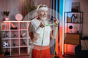 Strong older man using resistance band for training at home