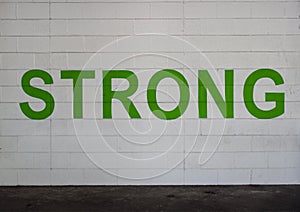 STRONG is painted in bold green letters on a white brick wall in the parking garage on Victory Park Lane, Dallas, Texas