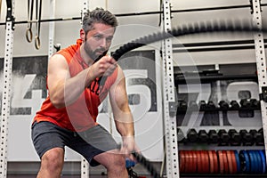 Strong powerful man working out with battle ropes at gym, developing strenth and endurance.