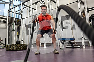 Strong powerful man working out with battle ropes at gym, developing strenth and endurance. photo