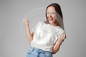 Strong powerful young woman raises arms celebrating success on gray background