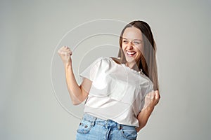 Strong powerful young woman raises arms celebrating success on gray background