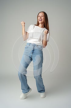 Strong powerful young woman raises arms celebrating success on gray background