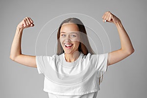 Strong powerful young woman raises arms celebrating success on gray background