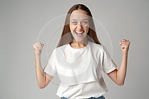 Strong powerful young woman raises arms celebrating success on gray background