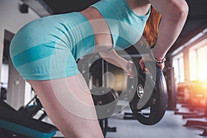 Strong pretty slim red-haired woman doing exercise with disks in gym