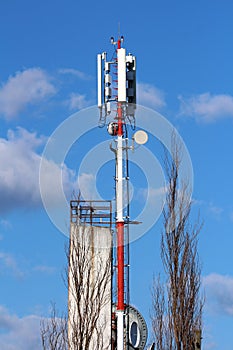 Strong red and white metal pole with various shapes and sizes cell phone transmitters and antennas next to tall building and
