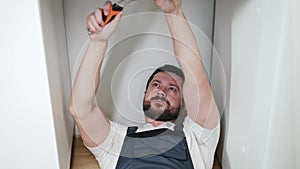 Strong repairman lying on floor and tightening valve with wrench while squinting