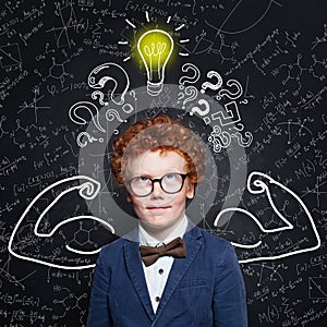Strong schoolboy kid with lightbulb on chalkboard background