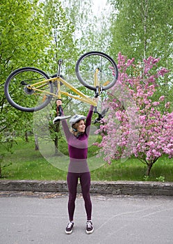 Strong slender young cyclist in a helmet lifts her bike cheerfully and vigorously over her head. cycling outdoors