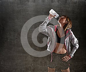 Strong sport freckles woman drinking water after training workout in gym club harsh light
